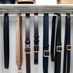 A sleek, minimalist closet with 7 belts neatly arranged on a wall-mounted organizer, showcasing a variety of styles and colors